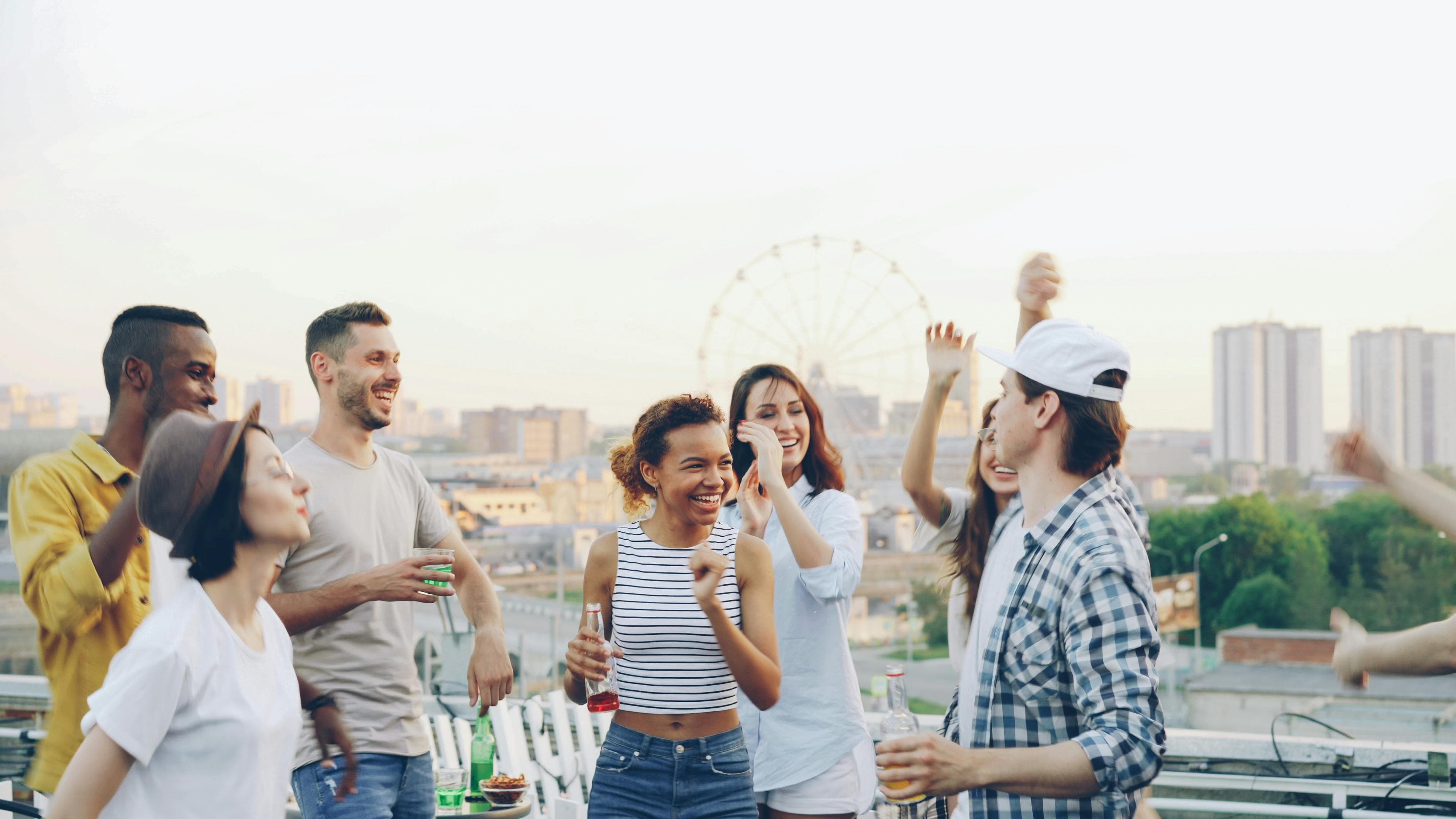 Two crews on a rooftop at golden hour, dancing and laughing with the city behind them